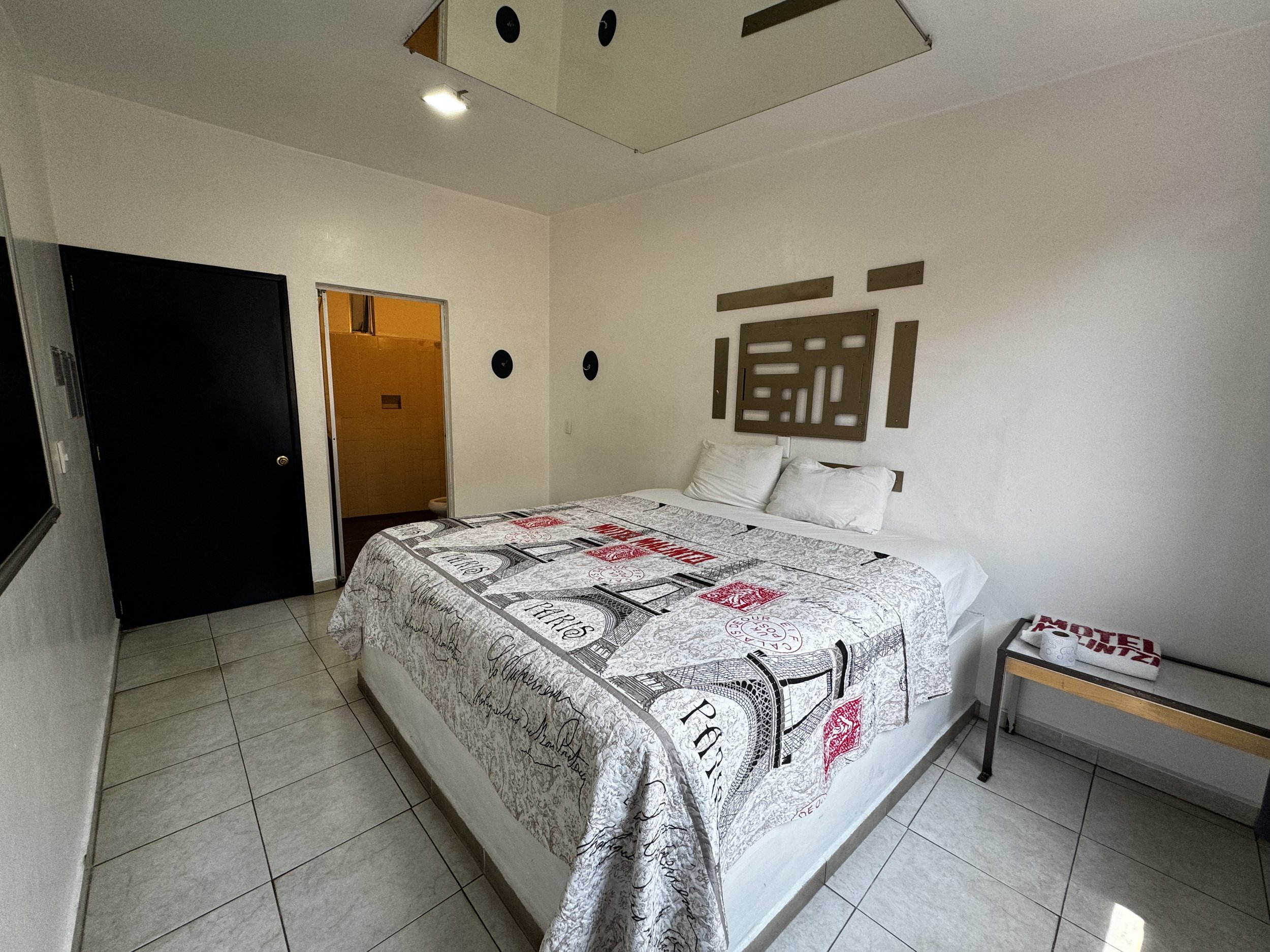 Habitación con colcha estampada, paredes blancas y acceso al baño