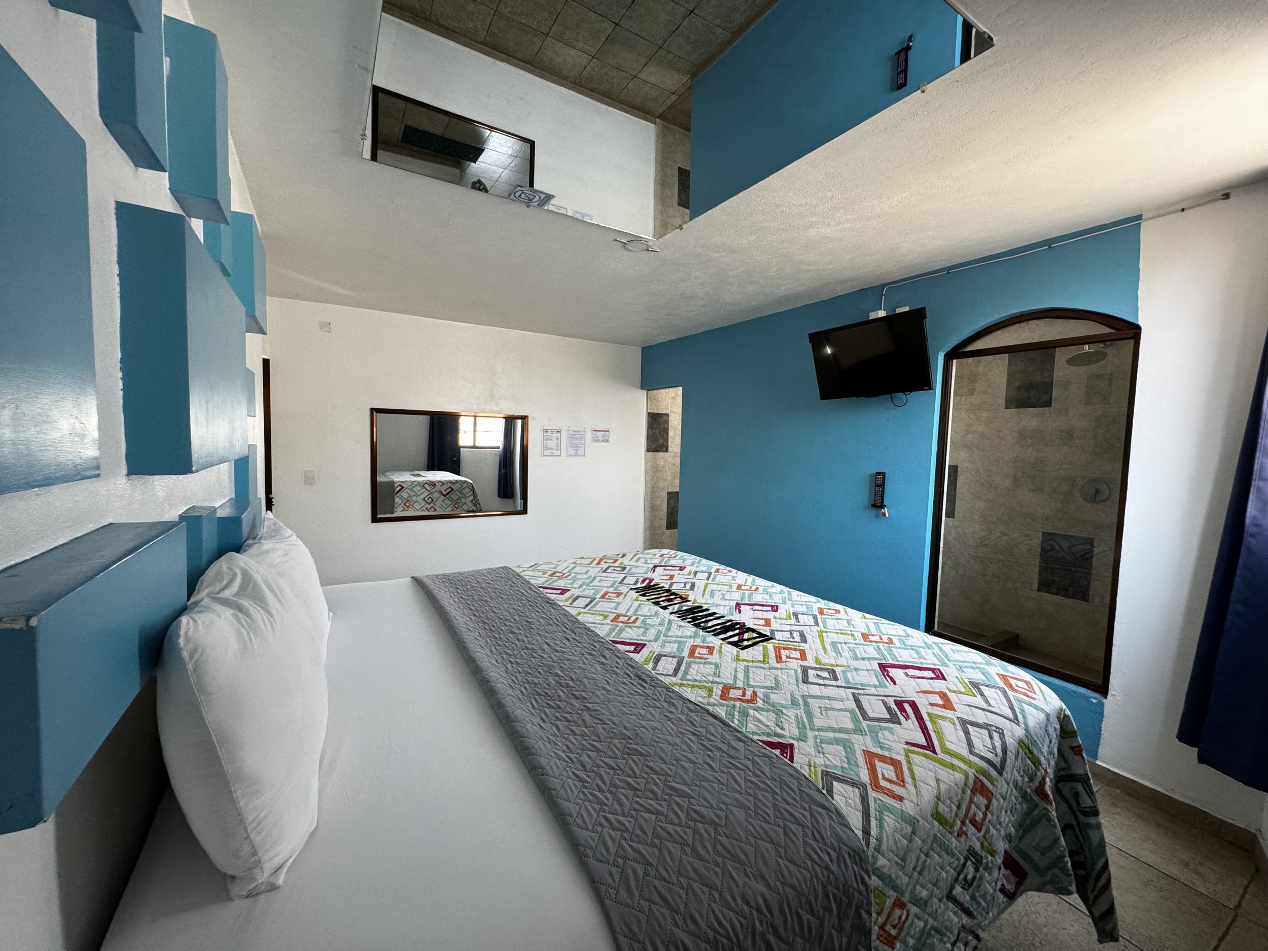 Habitación con cama grande, colcha colorida, paredes azules y espejo en el techo