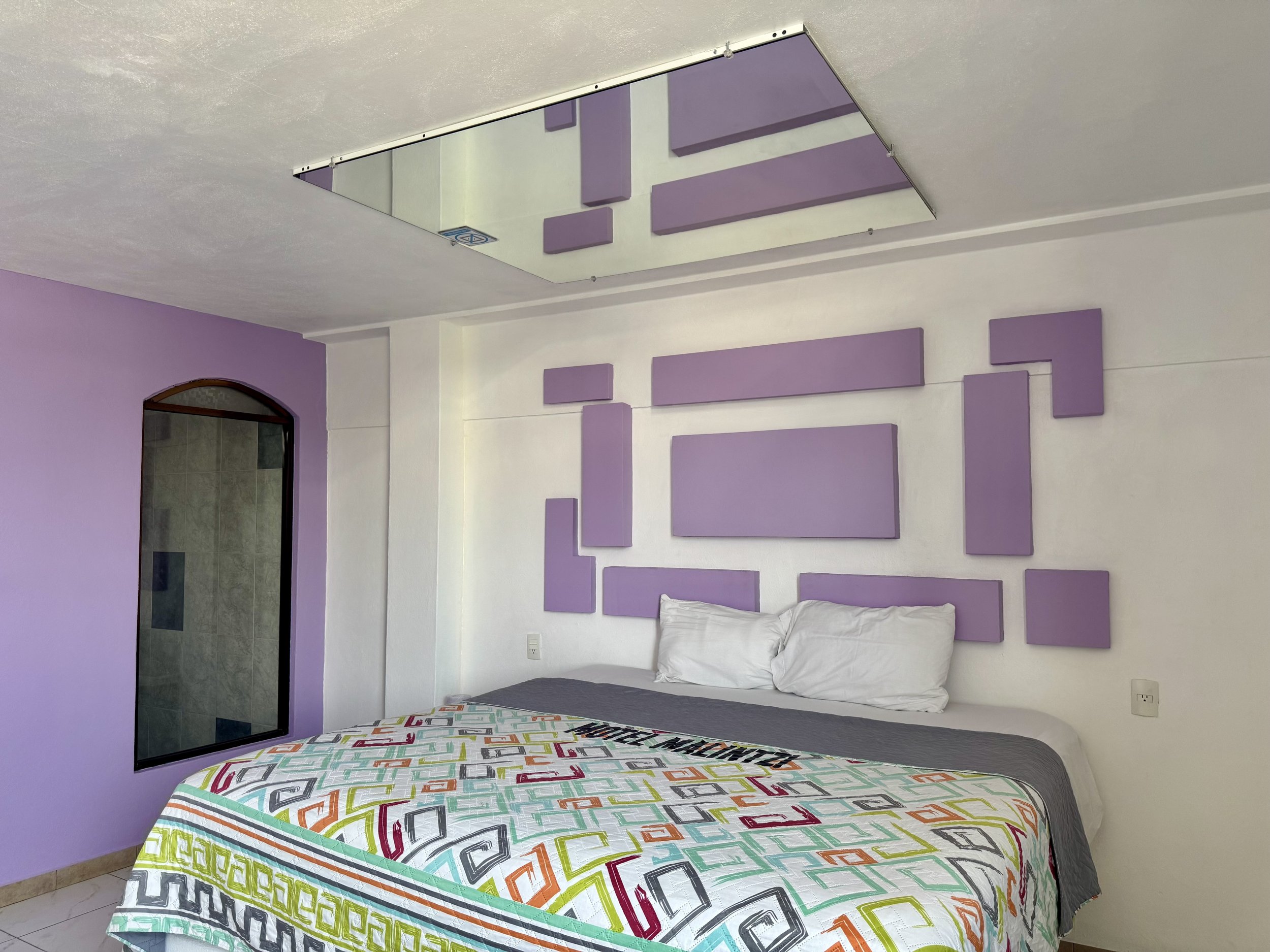 Habitación con pared morada, paneles geométricos y espejo en el techo