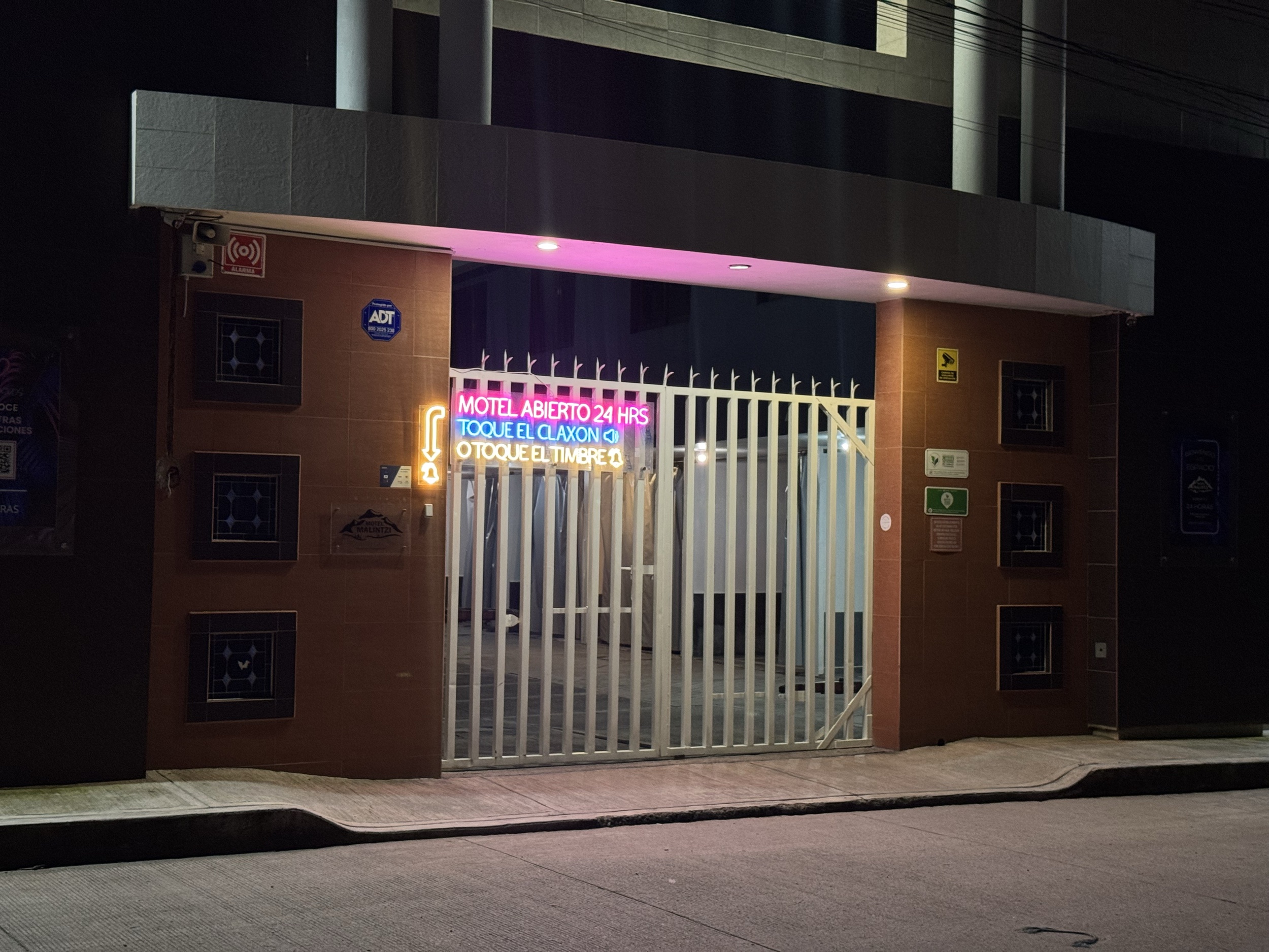 Portón de acceso de Motel Malintzi de noche con letrero de neón